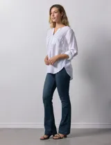 Blusa blanca de lino y rayón, con cuello a la base, escote en V y abertura con botones. Tiene bolsillos en la parte delantera y mangas largas regulables con presilla y botón.