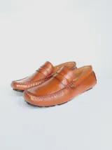 Zapato tipo mocasín driver de cuero color marrón claro, con antifaz y suela de goma negra.