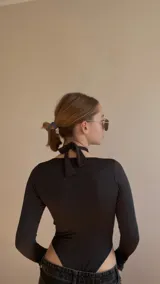 Body negro de lycra con escote cruzado y abertura en el pecho, atado atrás en el cuello y mangas largas.