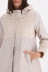 Pilotín largo con capucha, diseño combinado con secciones en matelassé en el pecho, mangas y ruedo. Cuenta con cierre frontal, bolsillos laterales y cordones ajustables en la capucha.