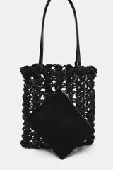 Bolso tipo shopper pequeño de crochet negro, con asas de hombro de material liso negro y una bolsa interior con cierre de cremallera.