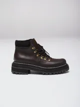 Botas acordonadas de estilo montañés, confeccionadas en cuero marrón oscuro con detalles en gamuza al tono. Presentan una suela track robusta de goma negra con costura visible y ganchos metálicos para los cordones.