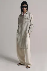 Vestido midi estilo camisero de Zara Woman Collection, confeccionado en lino, con estampado de rayas verticales azules sobre fondo beige. Cuenta con cuello solapa, escote en V con botonadura parcial, manga larga con puños abotonados, un bolsillo de plastrón en el pecho y bajo redondeado.