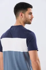 Remera de manga corta con diseño de bloques de color en tonos gris, blanco y azul marino. Cuenta con cuello redondo y una estampa tipográfica en el centro del pecho.
