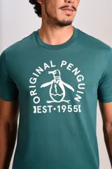 Remera de manga corta con cuello redondo, color verde oscuro, con estampa frontal del logo de la marca Original Penguin y la inscripción EST 1955 en color blanco.