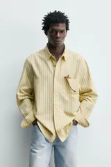 Camisa de corte regular fit de tejido de algodón, con diseño de rayas verticales amarillas y azules. Cuenta con cuello abotonado, manga larga con puños abotonados, un bolsillo aplicado en el pecho y cierre frontal con botones.