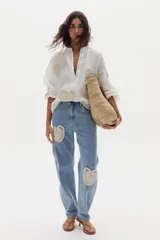 Pantalón estilo cargo confeccionado en denim celeste, de corte recto y holgado. Presenta apliques decorativos circulares de crochet en tonos beige en los laterales y bolsillos utilitarios.