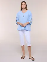 Blusa Erika de algodón con estampado de rayas en tonos azules, rosados y amarillos. Presenta cuello redondo con escote en V y botones frontales, mangas cortas decoradas con una fila de botones en los laterales y dobladillo asimétrico.