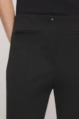 Pantalón capri negro de corte sastrero, confeccionado en tejido de punto grueso con elastano. Presenta calce slim, alforzas en el delantero, bolsillos ojal simulados, aberturas laterales en los bajos y cierre frontal con botón y broche metálico.