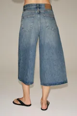 Bermuda de denim de tiro medio y corte wide leg, con diseño culotte, trabillas en la cintura y pliegues delanteros. Posee cinco bolsillos y cierre frontal con cremallera y botón.