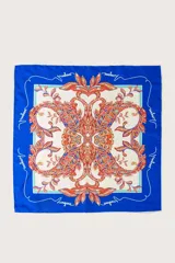 Pañuelo cuadrado de tejido ligero con estampado floral y botánico en tonos cálidos sobre fondo crema, enmarcado por un borde ancho en color azul vibrante con detalles de líneas blancas.
