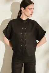 Blusa negra de lino de silueta amplia, con cuello mao y doble hilera de botones dorados en el frente. Cuenta con mangas cortas con vuelta.