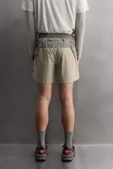 Pantalón corto de trail running color beige, confeccionado en tejidos técnicos ligeros y elásticos. Cuenta con forro interior, cintura elástica ajustable con cordón, bolsillos traseros laterales multifunción, bolsillo trasero central con cremallera, bajo con costura termofijada y aberturas laterales. Incluye logo estampado en la pernera.