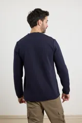 Remera de manga larga en tejido elastizado, color azul, con cuello tipo camisa, cartera con botones y detalles en eco gamuza en la base del cuello y la cartera.
