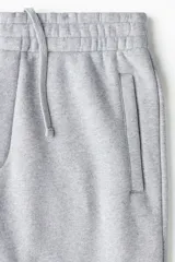 Pantalón deportivo de felpa de mezcla de algodón en color gris melange, con corte relajado, cintura elástica y puños ajustados en los tobillos. Cuenta con bolsillos laterales y cierre decorativo.