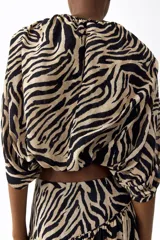 Pollera maxi de tiro alto confeccionada en gasa con estampado de cebra en tonos beige y negro. Cuenta con cintura ancha y costura fruncida en diagonal.