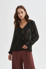 Blusa blanca de poliéster con cuello en V, volados frontales y mangas largas con elástico en los puños.