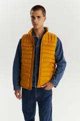 Chaleco puffer acolchado color mostaza, con cuello alto y cierre frontal. Diseño ligero y versátil con bolsillos laterales.
