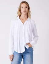 Camisa blanca de rayón con cuello solapa, escote en V y cierre frontal con botones. Presenta plisados verticales en la parte delantera y un canesú con tablón central en la espalda. El bajo es redondeado y ligeramente más largo en la espalda.