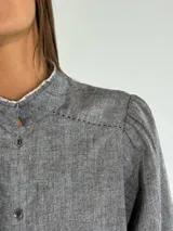 Camisa color beige con cuello mao, mangas largas abullonadas y cierre frontal con botones.