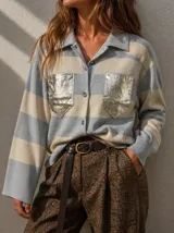 Camisa de punto a rayas horizontales en tonos celeste y crema, con cuello camisero, cierre frontal de botones y bolsillos frontales con acabado metalizado plateado.