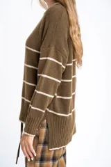 Sweater de lana con diseño de rayas horizontales blancas sobre fondo verde oliva. Presenta cuello redondo, mangas largas con puños acanalados y un corte oversize con tajos laterales en el ruedo.