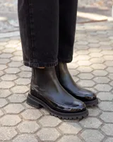 Botinetas tipo Chelsea de cuero negro, con paneles laterales elásticos y suela track dentada de goma. Presentan una combinación de texturas entre cuero mate y cuero charolado en la puntera y el talón.