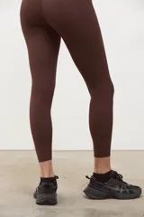 Calza deportiva de tiro alto color marrón espresso, confeccionada en tejido suave y elastizado con compresión media. Presenta un diseño sin costuras en el frente, largo 3/4 y terminaciones con corte láser en las piernas.