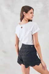 Remera negra de algodón peinado, ajustada al cuerpo, con cuello redondo y detalles de vainillas caladas en el escote y los hombros. Las mangas son cortas y están dobladas hacia afuera.