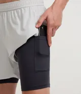Bermuda deportiva verde militar con short de compresión incorporado, cintura elástica y cordón ajustable, confeccionada en microfibra de poliéster y elastano.