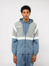 Campera de nylon Umbro con capucha, cierre frontal y diseño de bloques de color en gris, blanco y azul. Puños y dobladillo elásticos.