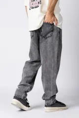 Jean de corte mom oversize, color negro lavado, con diseño de cinco bolsillos y cierre frontal con botón y cremallera.