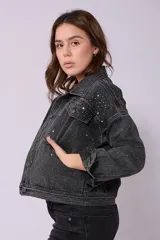 Campera de jean de mujer, color negro lavado, con corte holgado y manga larga. Presenta apliques de brillos plateados distribuidos por toda la prenda, cuello camisero y bolsillos delanteros con tapa y botón.
