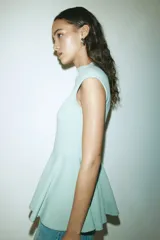 Top entallado de punto roma color verde menta, con diseño sin mangas de hombros cubiertos, cuello alto y corte peplum con vuelo en la parte inferior.
