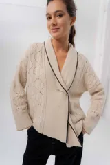 Saco tejido de lana color beige, con diseño cruzado tipo kimono, cuello smoking con ribete en contraste oscuro, mangas largas y tramas caladas.