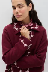 Chaqueta de lana merino hervida en color marrón, con diseño estructurado y cuello amplio. Presenta detalles de bordado artesanal en contraste color mostaza a lo largo del frente, cuello y puños, junto con botones forrados en la misma tela.