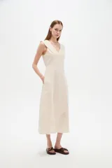 Vestido midi color beige claro, con cuello en V, sin mangas y corte entallado con pinzas.