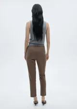 Pantalón de tiro medio con diseño crop, corte skinny y estampado a cuadros tipo tartán en tonos marrones y negros. Cuenta con trabillas en la cintura, bolsillos laterales y cierre oculto con botón, gancho y cremallera.