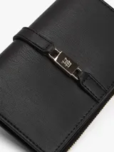 Billetera bifold de Tommy Hilfiger en color negro, confeccionada en poliuretano con acabado texturizado. Presenta un cierre principal con cremallera y una solapa frontal con un detalle metálico distintivo de la marca con el logo TH.
