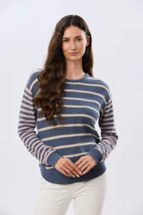 Buzo tejido de algodón con diseño a rayas horizontales, cuello redondo y mangas largas. El cuerpo presenta rayas en tonos azul y beige, mientras que las mangas combinan rayas en tonos azul y rosado.