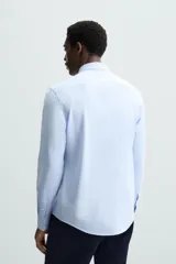 Camisa de manga larga, color celeste con finas rayas verticales blancas, cuello italiano y cierre frontal de botones.