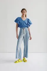 Pantalón de jean de corte recto y tiro alto, confeccionado en una combinación de dos tonos de denim. Presenta un cierre frontal metálico visible y costuras decorativas verticales que recorren el largo de las piernas.