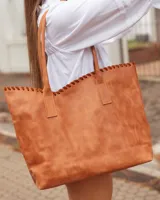 Bolso tipo shopper de cuero, color marrón tostado, con detalle de costura artesanal en el borde superior y correas largas para llevar al hombro.
