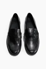 Mocasines estilo penny de color negro, con costura tradicional en la parte delantera y suela baja.