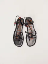 Sandalias planas de cuero color marrón, con diseño de punta cuadrada, tiras finas cruzadas y un detalle trenzado circular en el empeine. Cuentan con tiras para atar al tobillo decoradas con cuentas turquesas en las puntas.