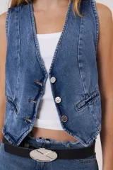 Chaleco de gabardina color blanco, con escote en V, cierre frontal con botones y bolsillos delanteros simulados.