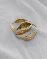 Brazalete rígido de diseño orgánico con textura irregular y acabado brillante, elaborado artesanalmente en metales nobles.