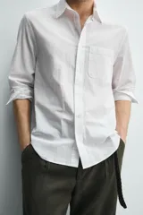 Camisa de corte regular fit color blanco, confeccionada en tejido de algodón con efecto arrugado, con cuello solapa, manga larga, puños abotonados y un bolsillo de parche en el pecho.