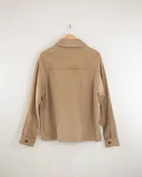 Camisa de pana color beige, de manga larga, con cuello camisero, cierre frontal de botones y dos bolsillos de parche con solapa en el pecho. Presenta un corte recto y holgado.