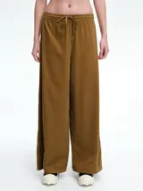 Pantalón de corte holgado y pierna ancha, confeccionado en pana color marrón. Presenta cintura elástica con cordón ajustable y diseño de tiro medio.